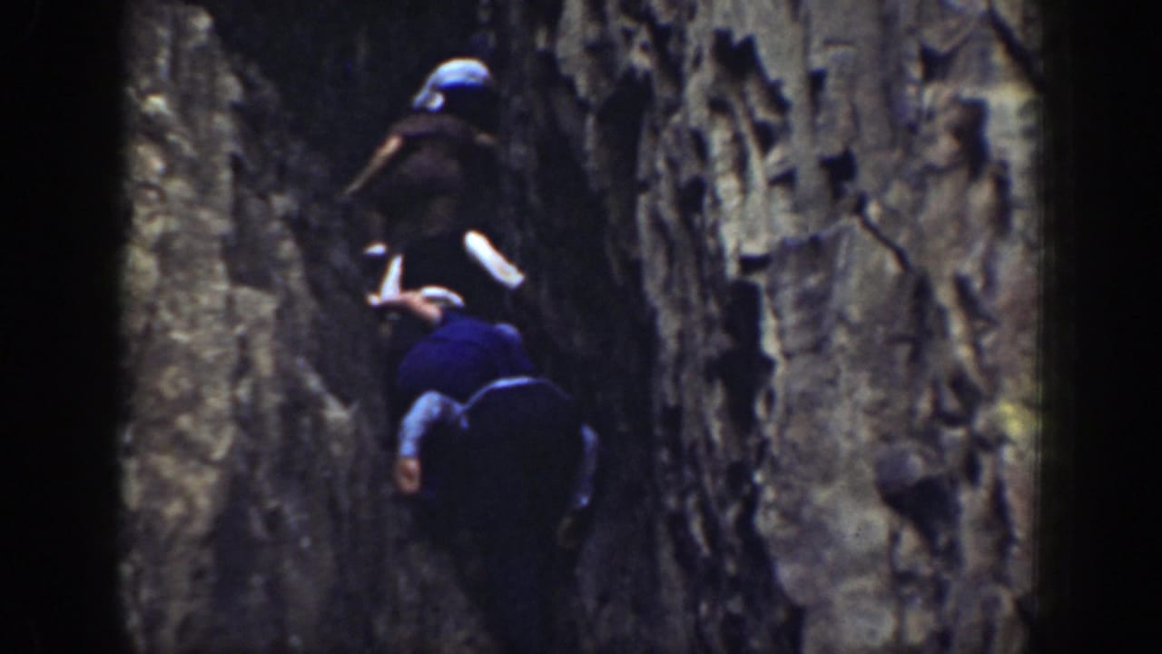 1937 California 8mm frame showing people in hats moving carefully through a shadowed rock crevice.
