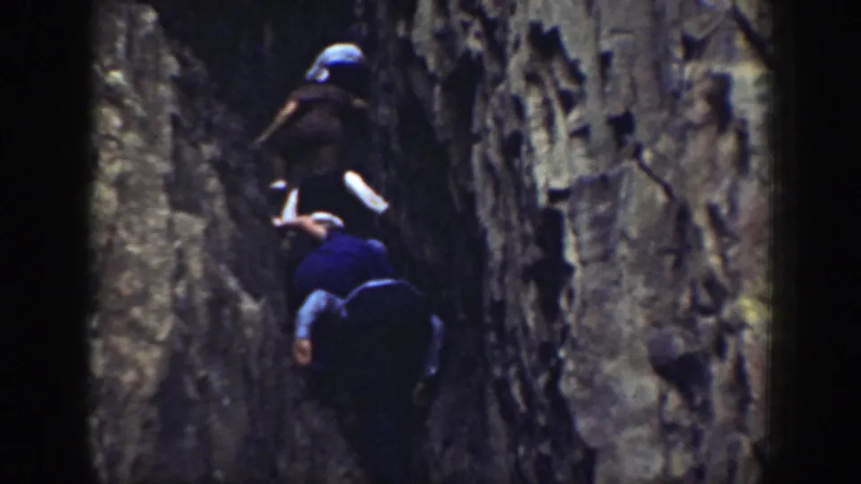 1937 California 8mm frame showing people in hats moving carefully through a shadowed rock crevice.