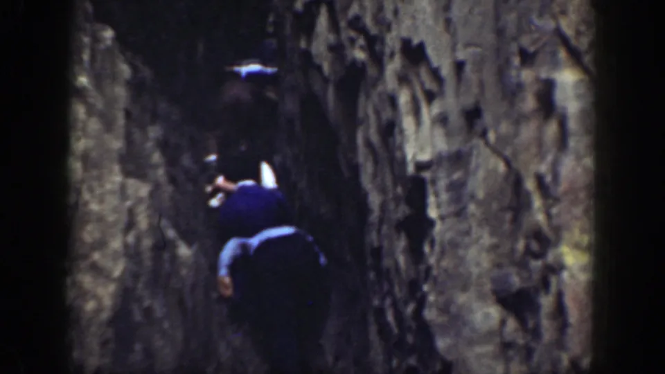 A handheld 8mm view of hikers moving deeper through a narrow rocky fissure in California.