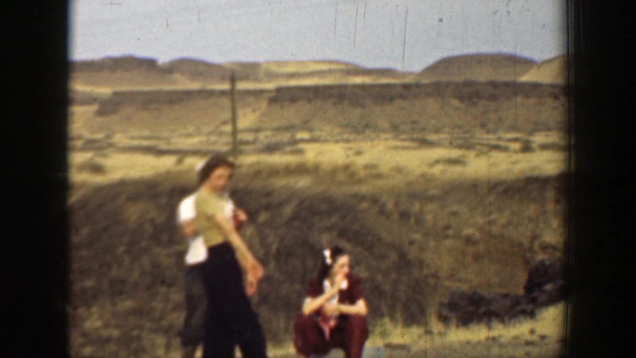 Adults outdoors in a dry hilly landscape, with one woman seated and others standing nearby.