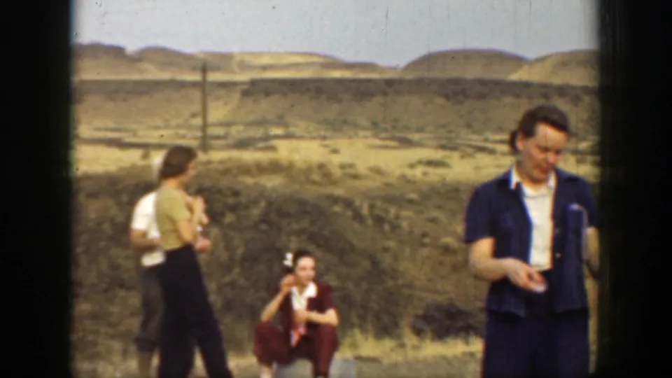 1937 California home-movie frame with a man in a blue jacket in the foreground and other adults gathered behind him in the desert setting.