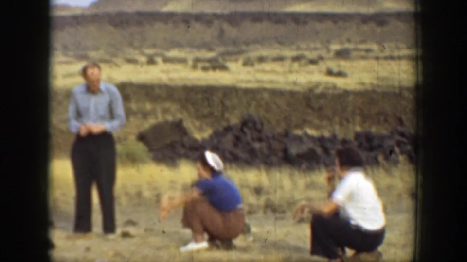 1937 California 8mm frame showing adults gathered casually in an arid outdoor area with low hills and rocky ground.