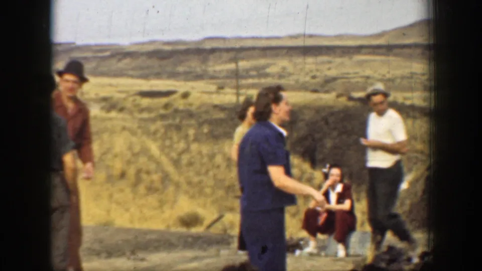 Group of adults in 1937 California home-movie footage gathered near a smoky fire in an arid landscape.