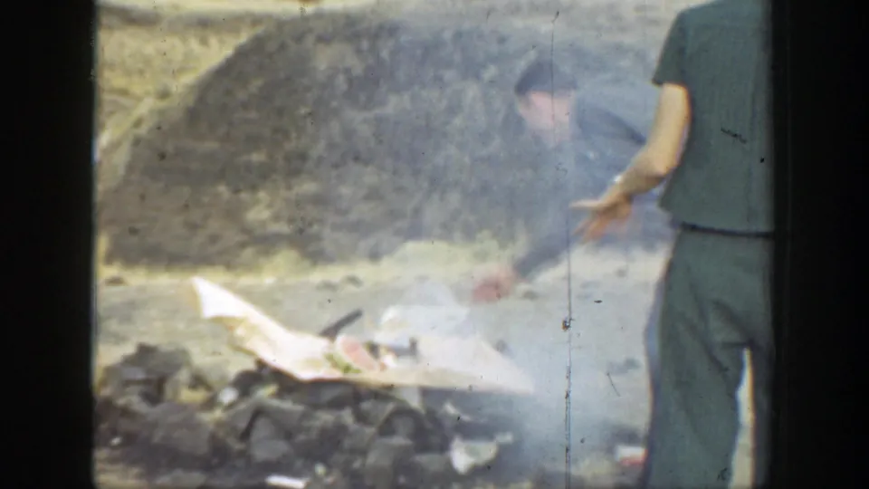 Soft 8mm frame from a 1937 California outdoor outing, with adults tending a smoky fire on dry ground.