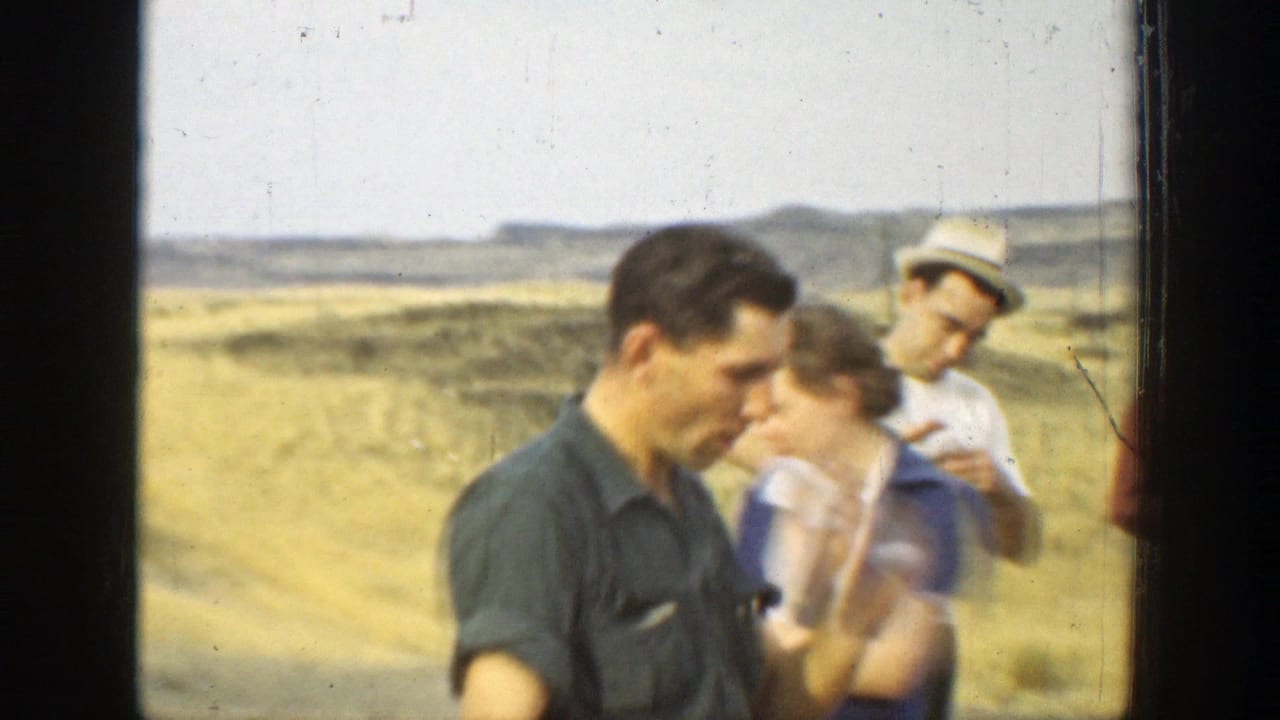 1937 California home-movie frame of adults gathered outdoors in dry hills, one man in a dark shirt looking down as others stand behind him.