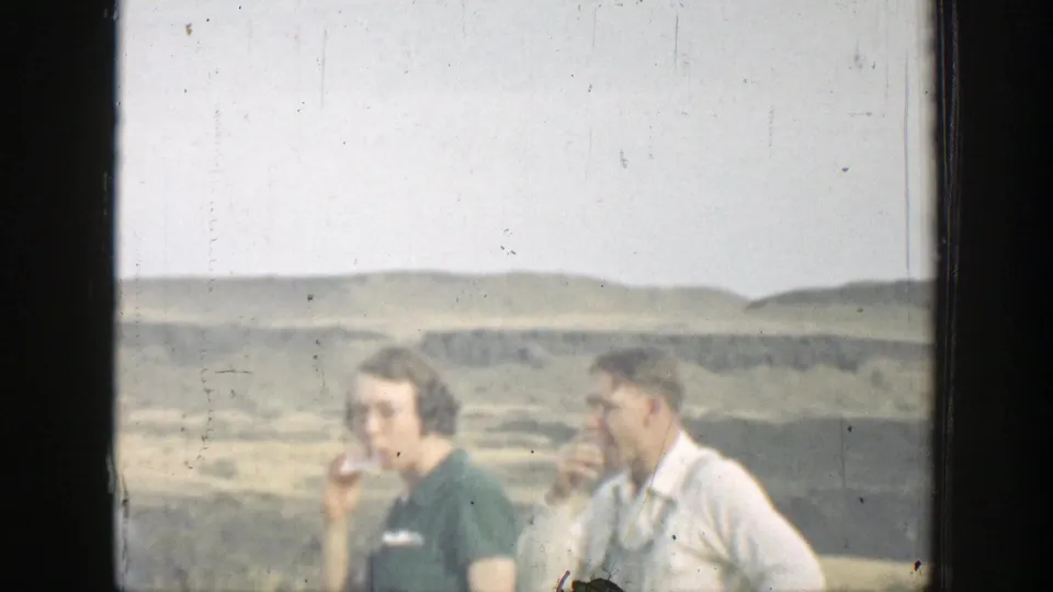 Two adults in 1937 California footage stand in front of dry rolling hills, with one figure appearing to smoke while another stands nearby.