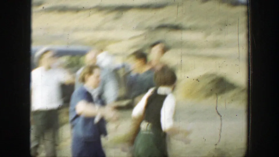 A soft 8mm frame shows several adults near a parked car in a dry California landscape, with motion blur from the handheld camera.