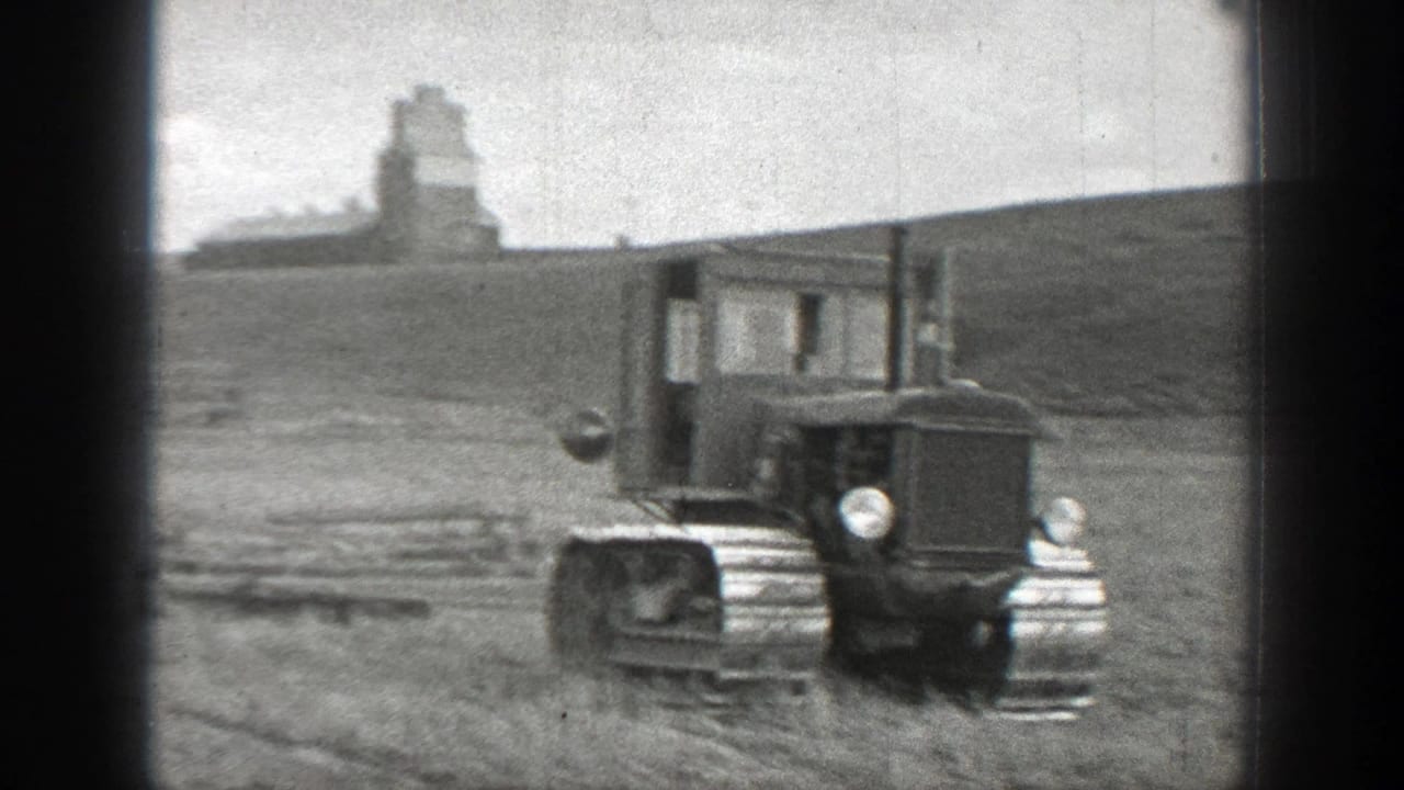 1937 California home-movie frame showing a tracked tractor in an open rural field, with a distant farm structure or silo on a low hill.