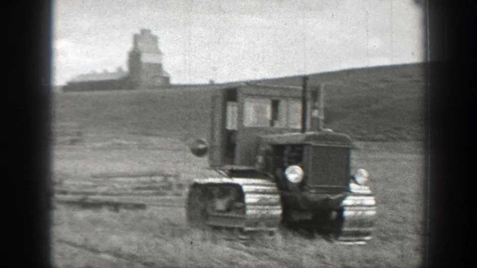 1937 California home-movie frame showing a tracked tractor in an open rural field, with a distant farm structure or silo on a low hill.
