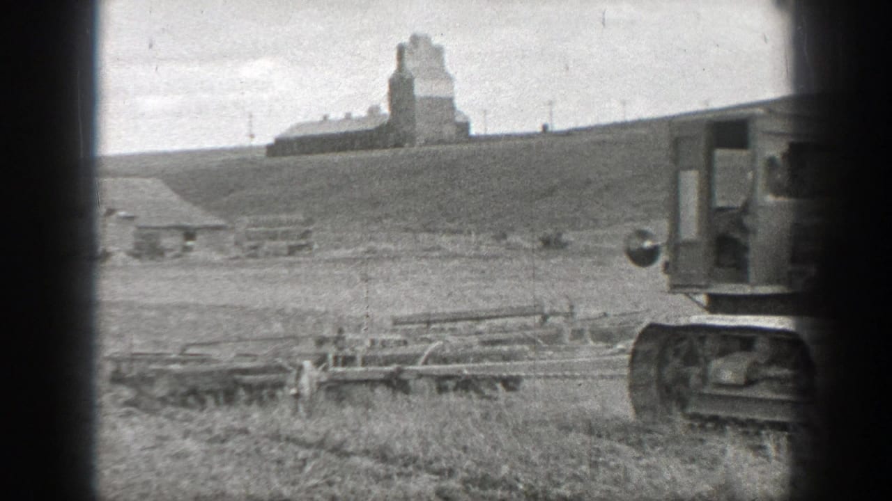 Tracked tractor partly at the right edge of a field with fences and a distant structure.