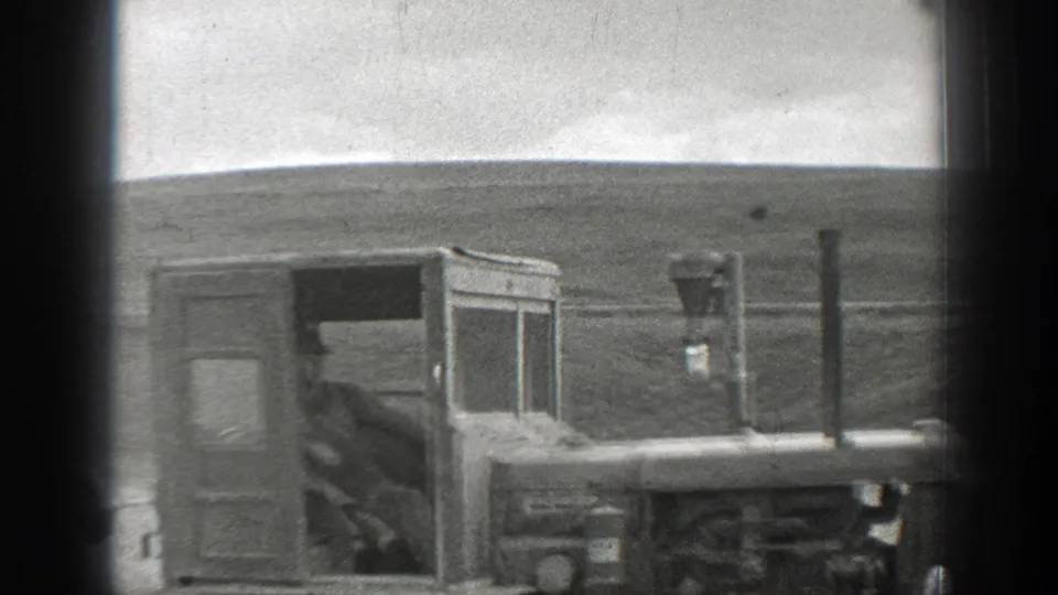 Side view of the tracked tractor in a California rural field, with the operator visible through the cab and low hills in the background.