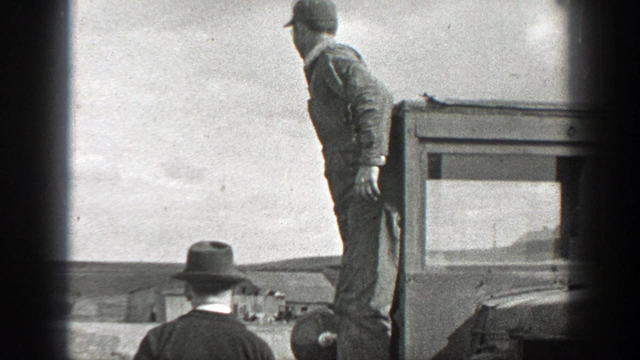 1937 California home-movie frame showing a man standing on a truck bed with another hat-wearing man below in an open outdoor setting.