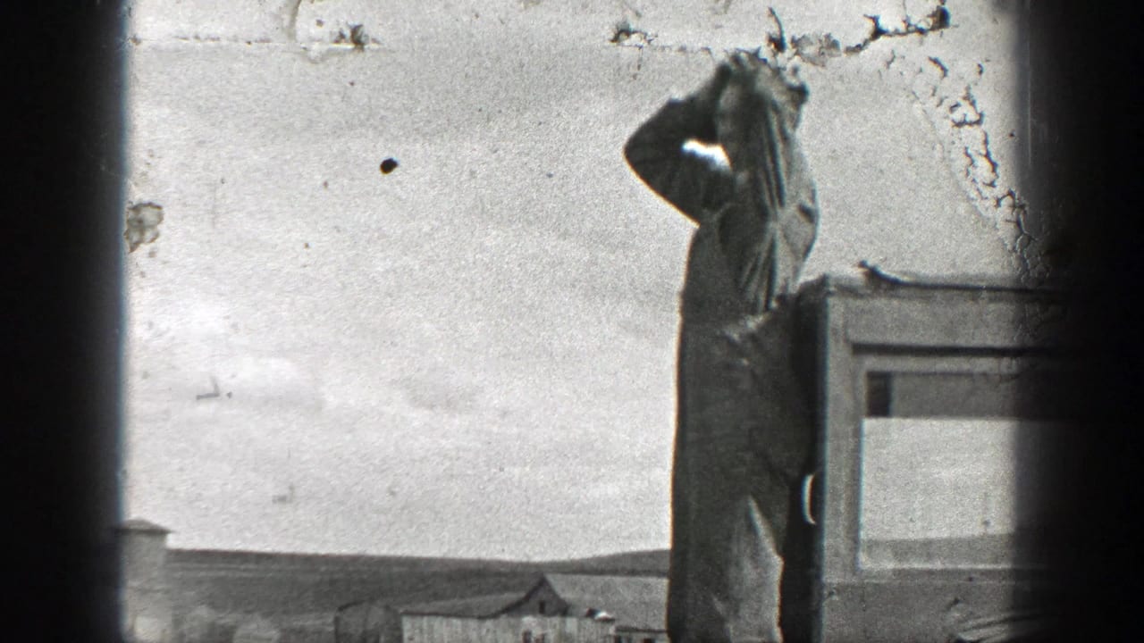 Man in work clothes stands beside a vehicle and raises a hand to his head outdoors.