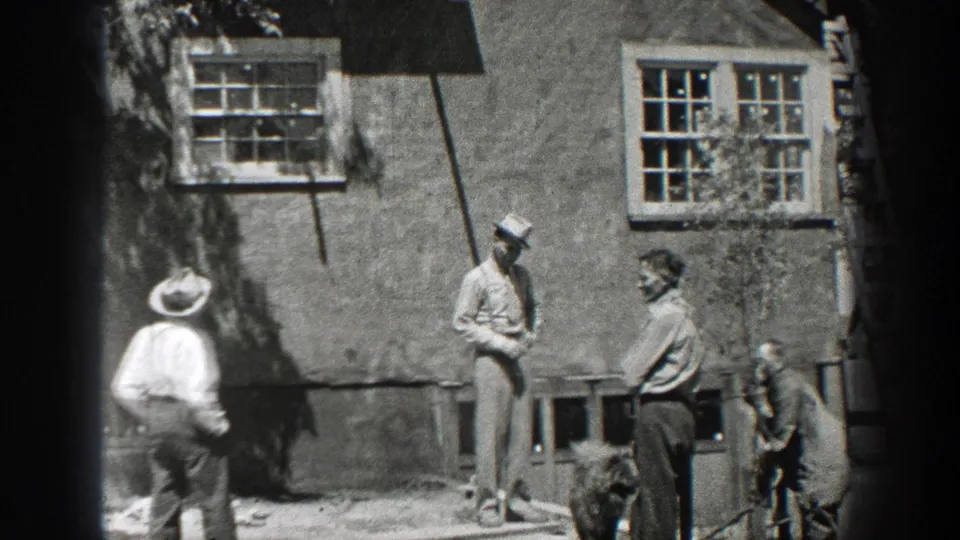 1937 California frame showing men in hats gathered outside a rustic building with windows, apparently taking a work break.