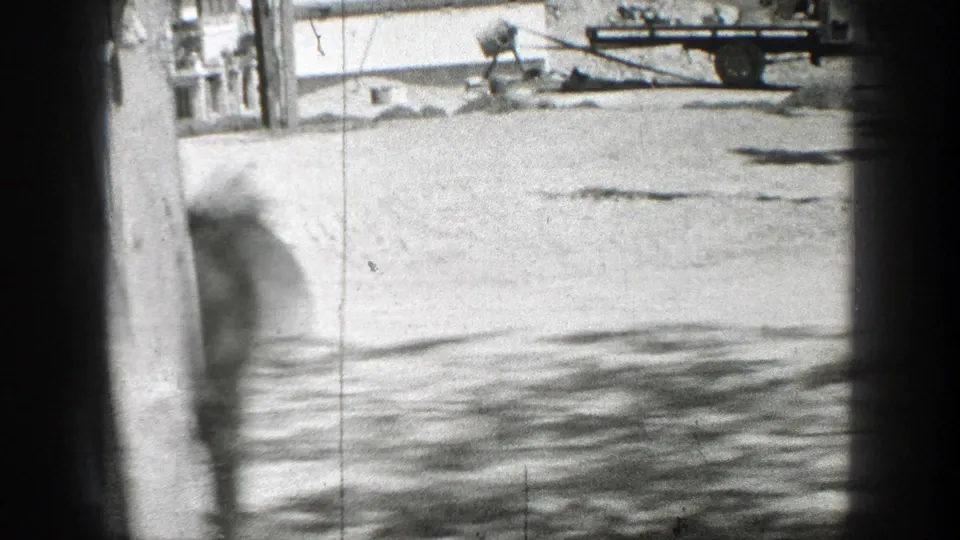 1937 California home-movie frame looking through dark window edges onto a bright yard with a blurred figure at left.