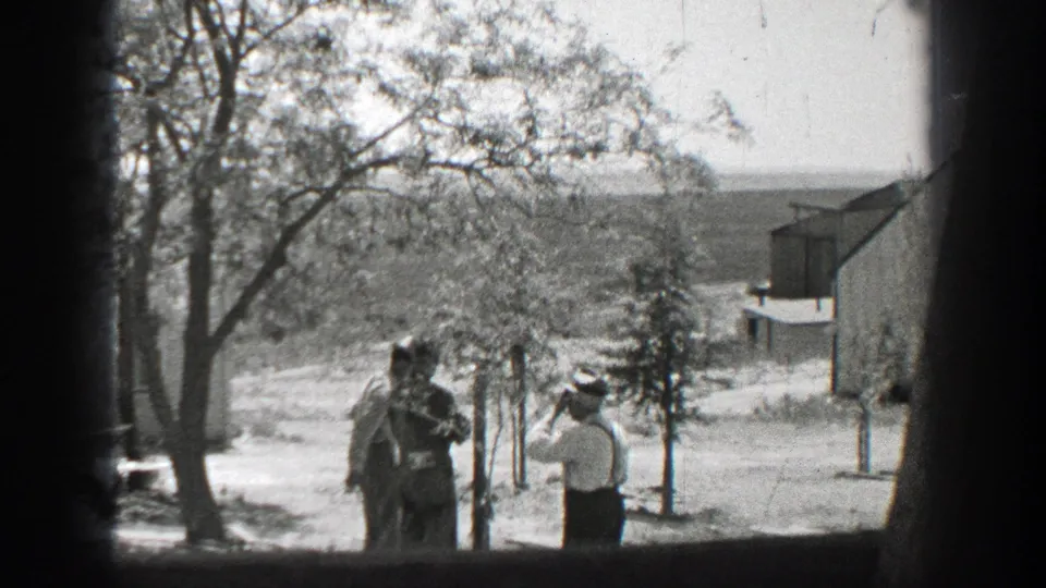 1937 California 8mm frame showing a man in a white shirt facing two men, one in uniform-like clothing, in a bright yard.