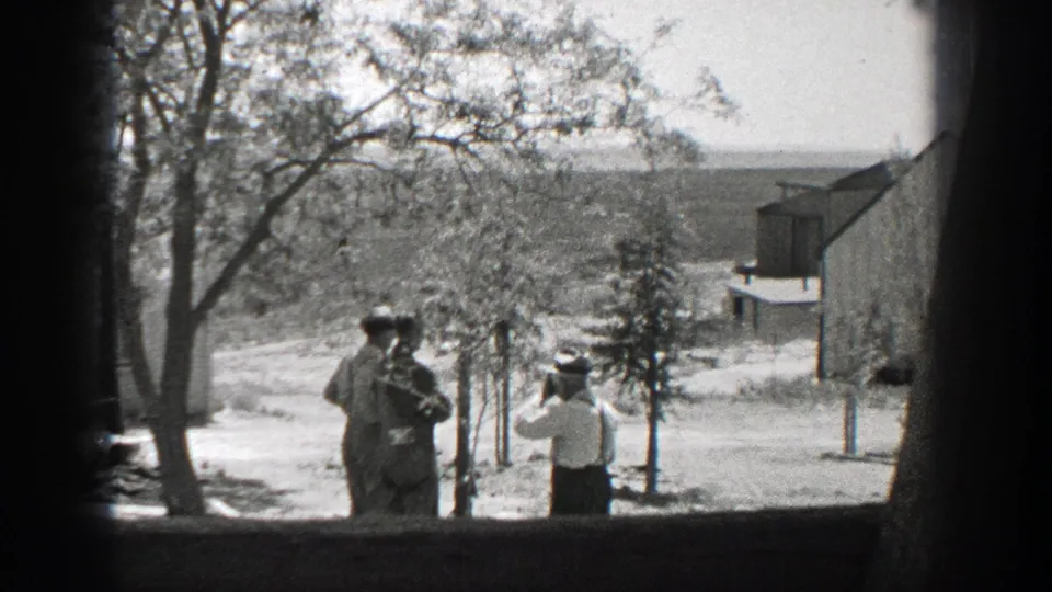 1937 California 8mm still showing two men near a tree and a white-shirted man at right in a sunlit yard.