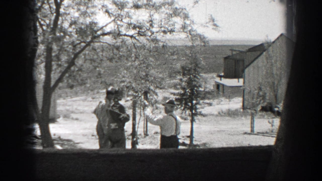 Two men stand in a yard seen through a dark window frame.