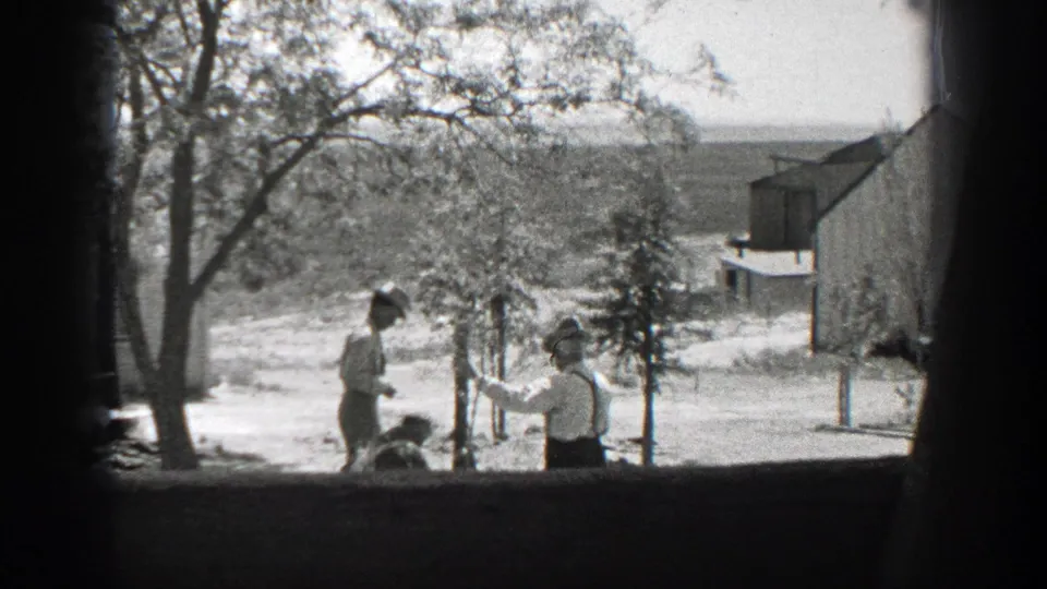 A woman carrying a bundle passes two men in hats beside a young tree in a California yard, seen in 1937 8mm footage.