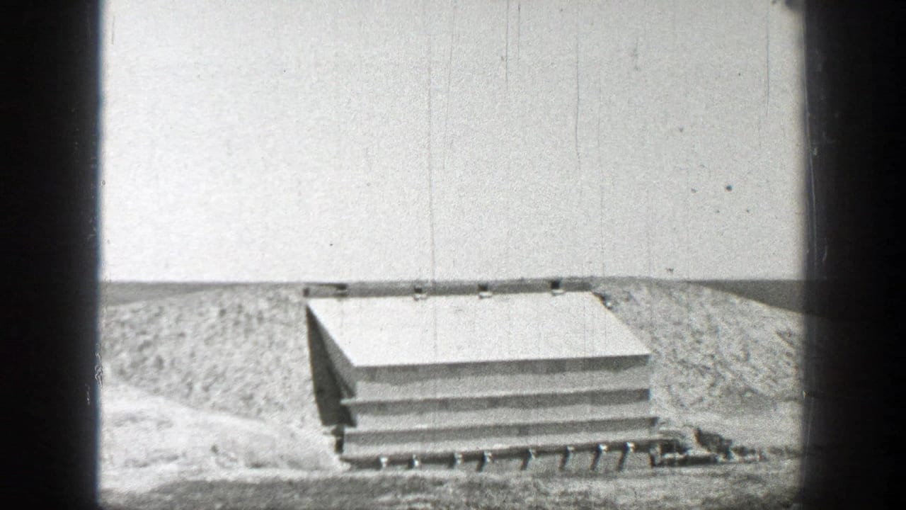 Low shelter-like structure partly set into sandy ground under an open sky.