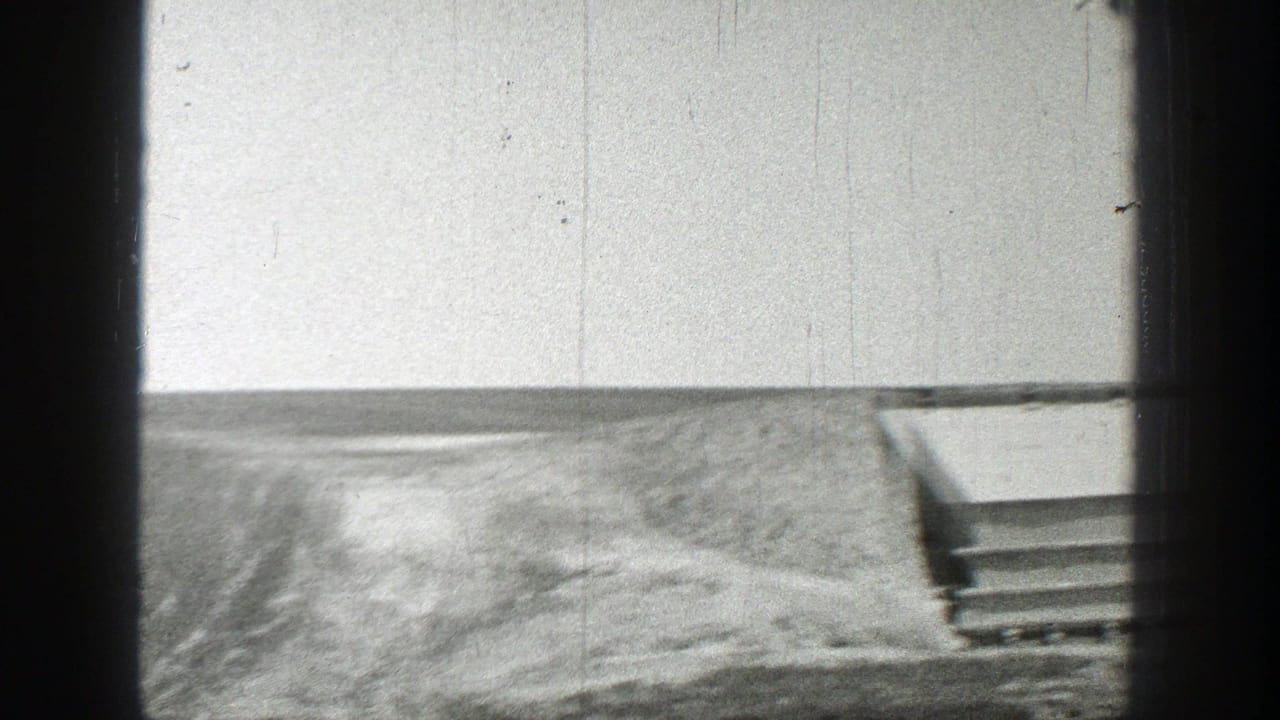 Open barren terrain with the edge of a shelter-like structure at right.