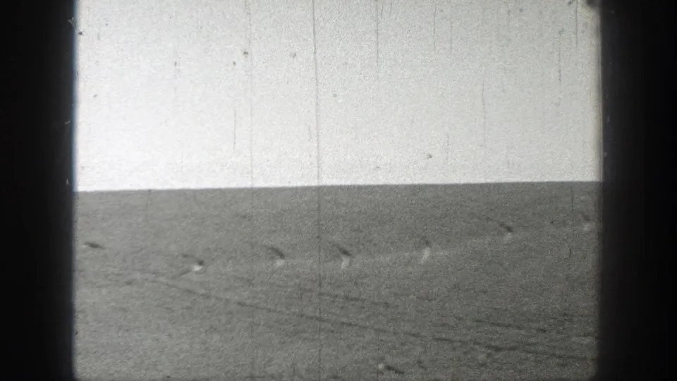 1937 California 8mm frame of empty, flat terrain under a pale sky, marked by vertical scratches and soft black-and-white exposure.