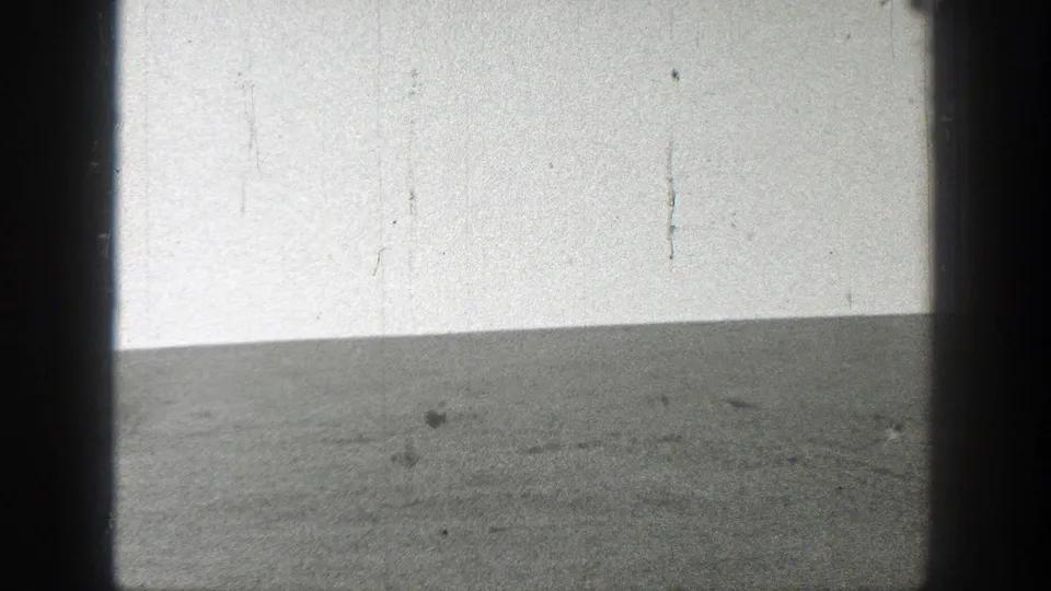 Black-and-white 8mm view of an empty California grass field with a low, slightly sloping horizon beneath a pale sky.