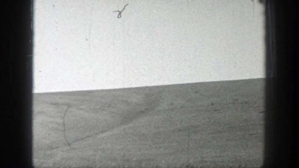 1937 home-movie frame of a sparse grassy slope under a bright sky, with 8mm gate borders and visible film wear.