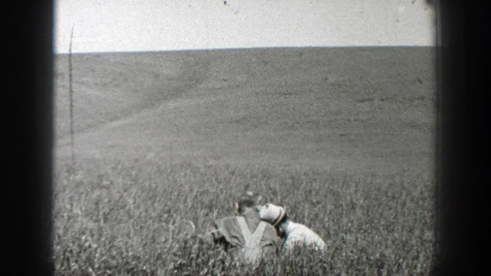 The man remains crouched in a California field, partly obscured by crop growth and framed by 8mm film edges.