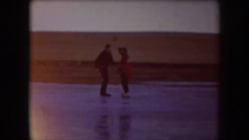 Two adults, one in a red jacket, hold hands while learning to skate on a frozen lake in North Dakota.
