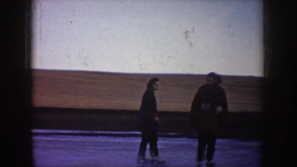 Two people appear on the frozen pond in North Dakota, one facing the camera area and one turned partly away near the ice edge.