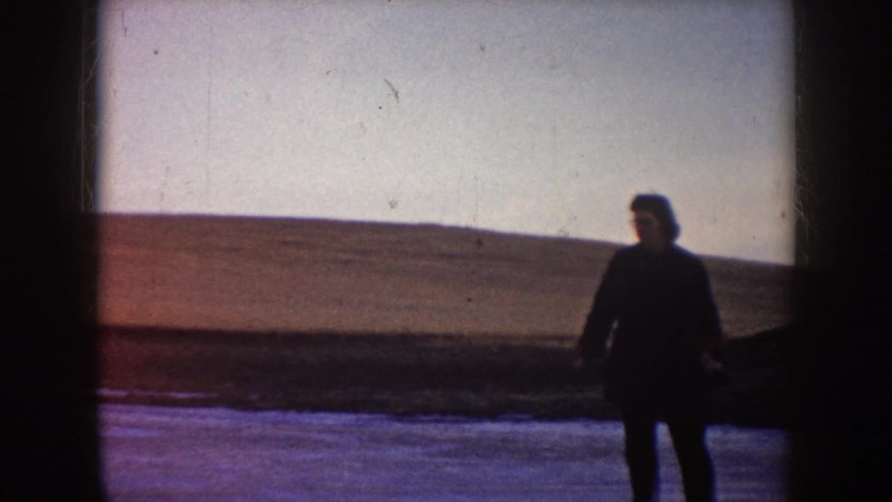 In supported 1953 North Dakota home-movie footage, a dark-coated person appears on a frozen lake against a pale sky and open shoreline.