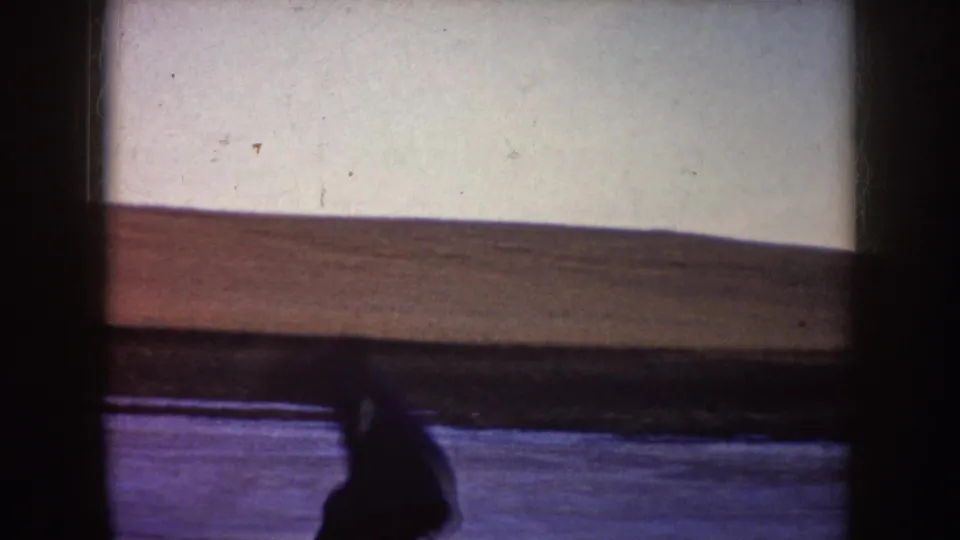 A person appears low on the frozen lake surface in the 1953 North Dakota winter scene, with the shoreline and pale sky in the background.