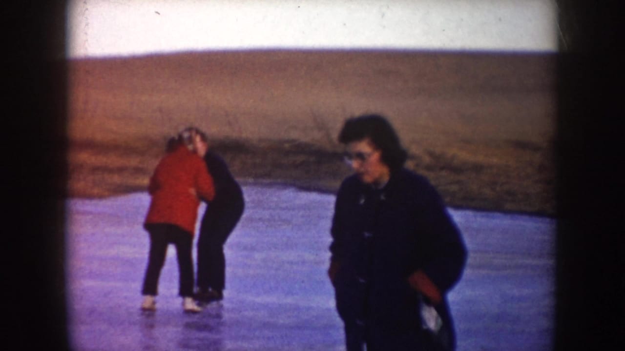 Two people skate on a frozen pond while another adult stands near the camera.
