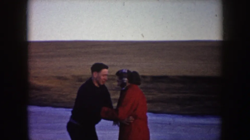 The skaters face each other on the frozen pond, the woman in a red coat and the man in dark clothing against the open North Dakota landscape.