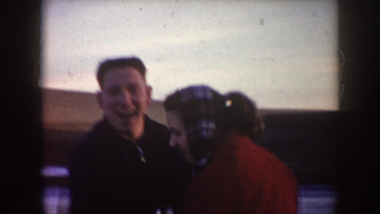 Man in a dark jacket smiles beside a woman in a red coat on outdoor ice.