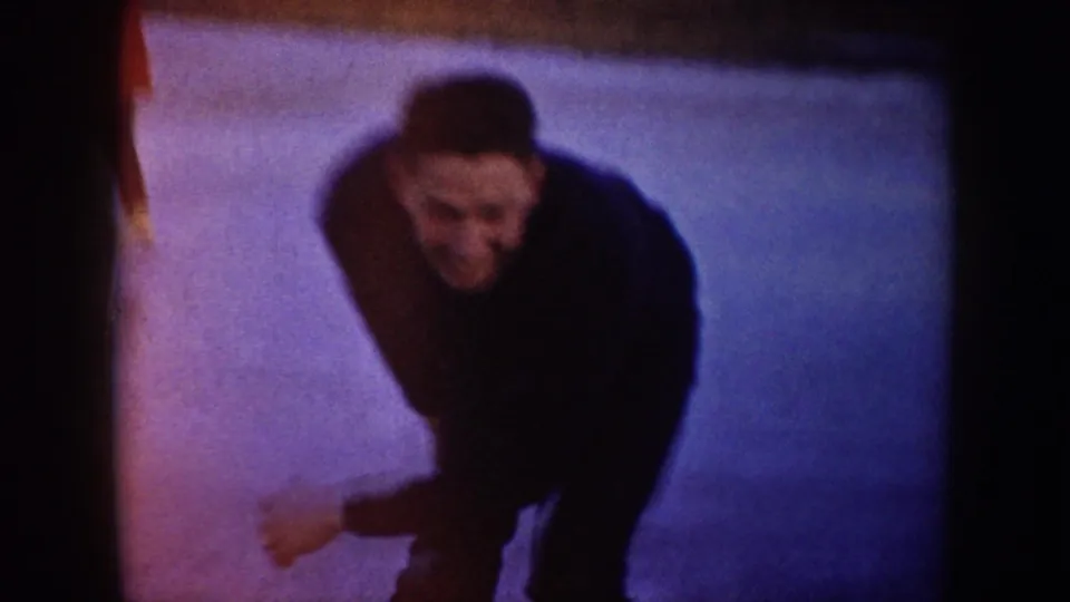 Close 1953 North Dakota home-movie frame of an adult man skating toward the camera on outdoor ice.