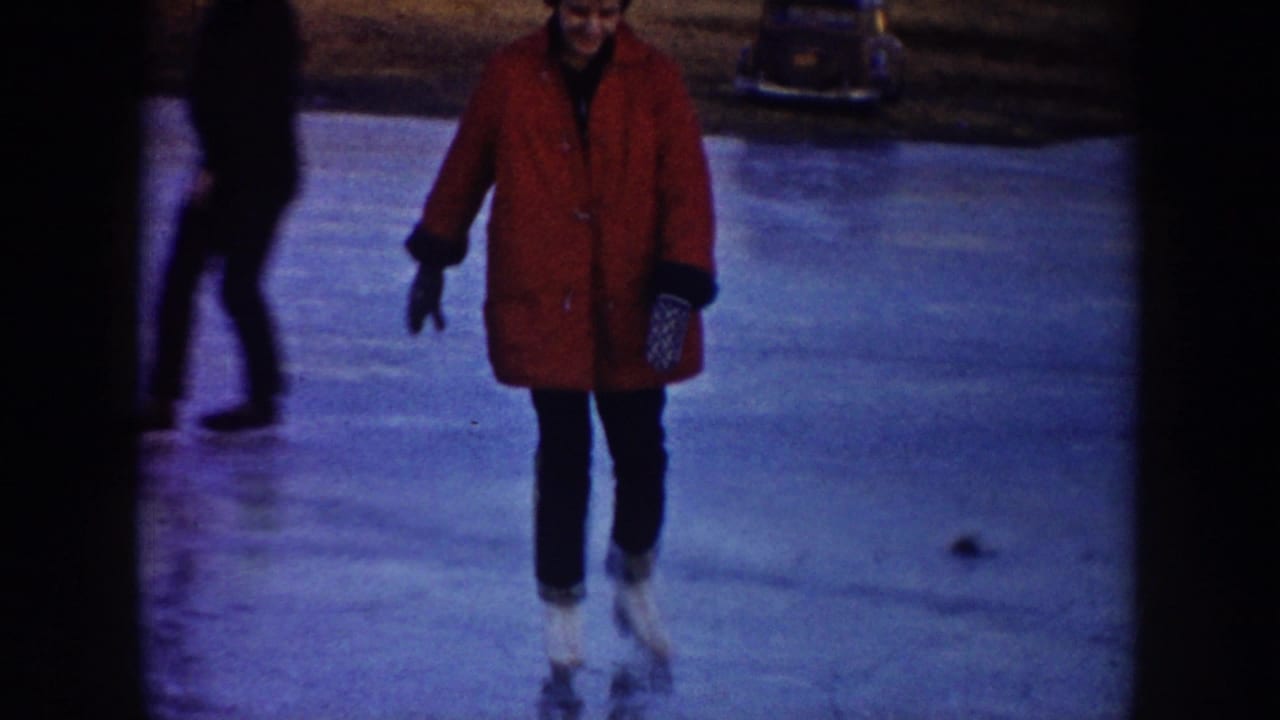 A woman in a red coat skates toward the camera on a North Dakota frozen pond as another person in dark clothing passes behind.