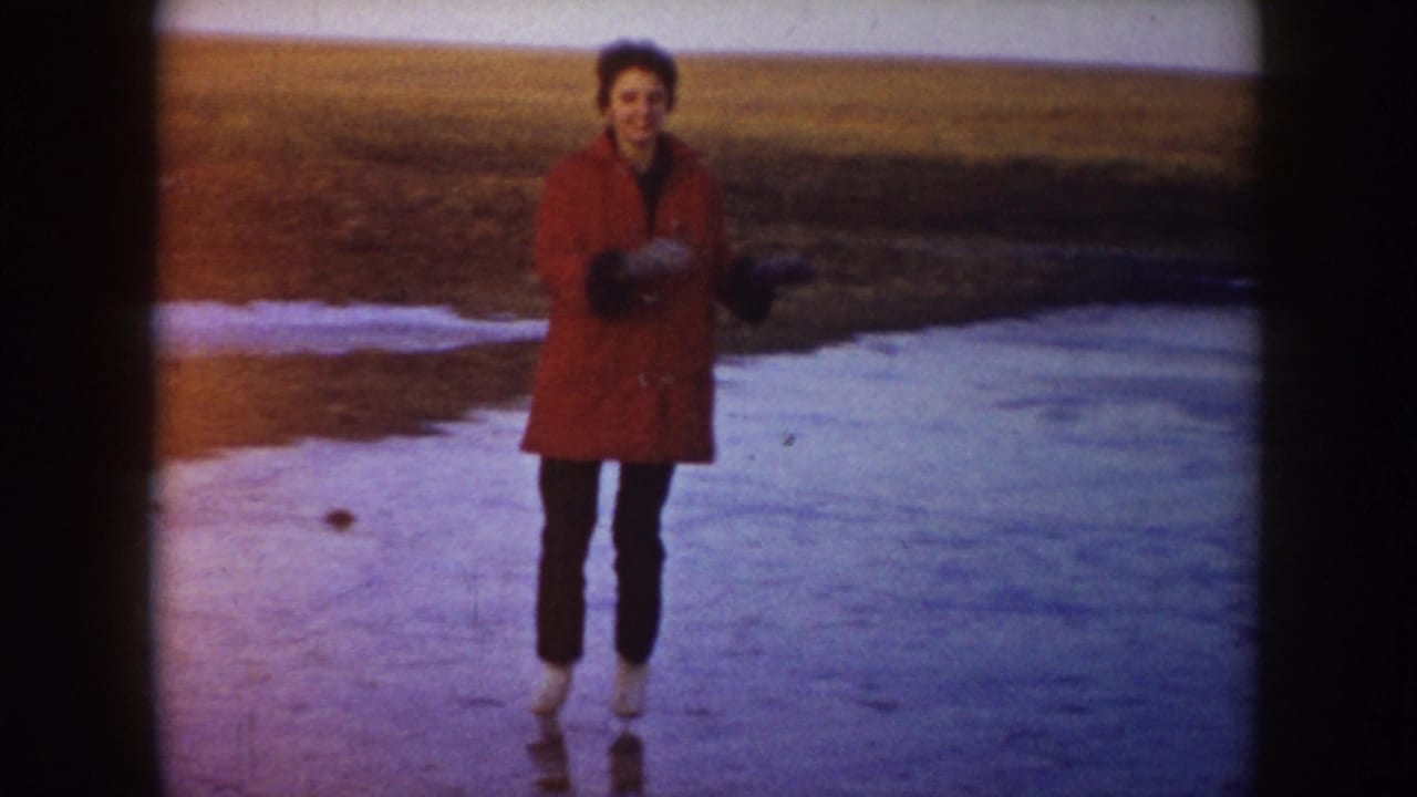 Woman in a red coat stands on skates on a frozen pond.