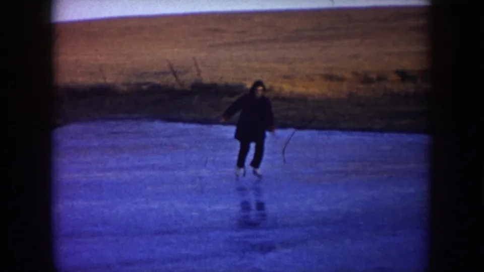 A skater moves across blue-toned ice near the pond edge, with open North Dakota grassland in the background.