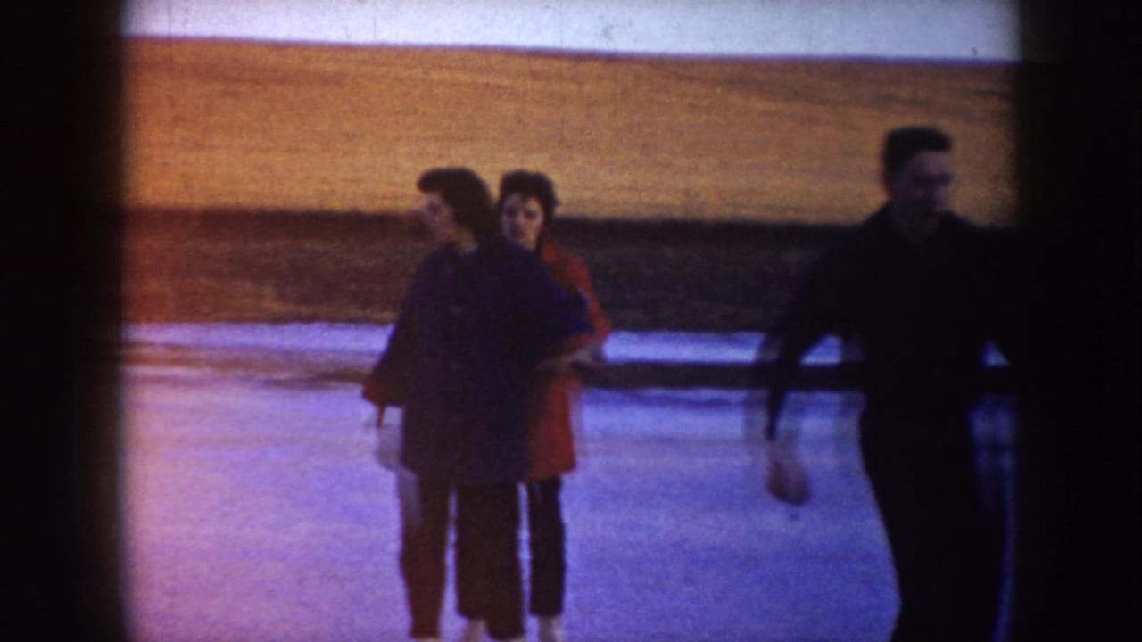 Two young women stand on a frozen pond as a man skates through the foreground in rural North Dakota.
