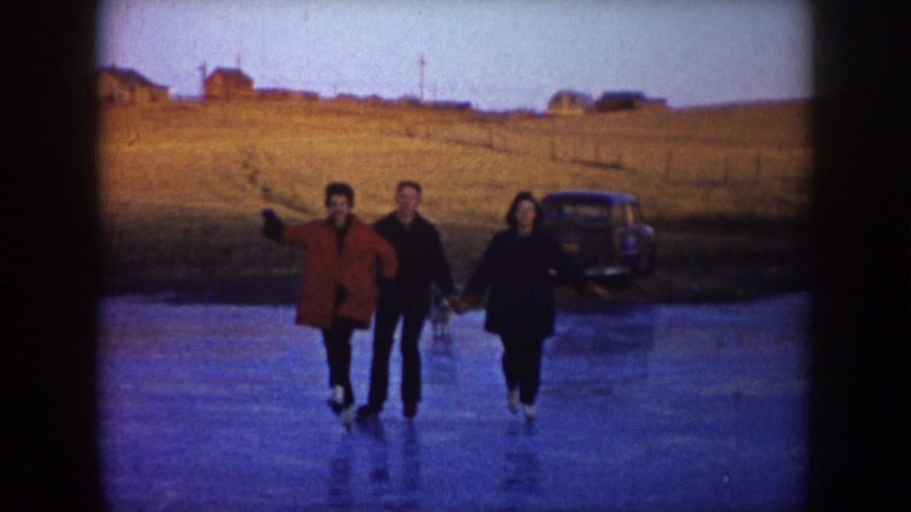 In 1953 North Dakota home-movie footage, three young people skate across a frozen pond with rural fields and a parked car in the background.