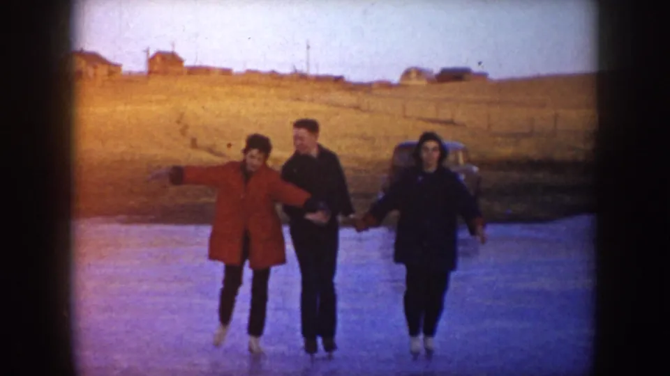 Three young people in winter coats skate toward the camera on a frozen pond in the supplied 1953 North Dakota setting.