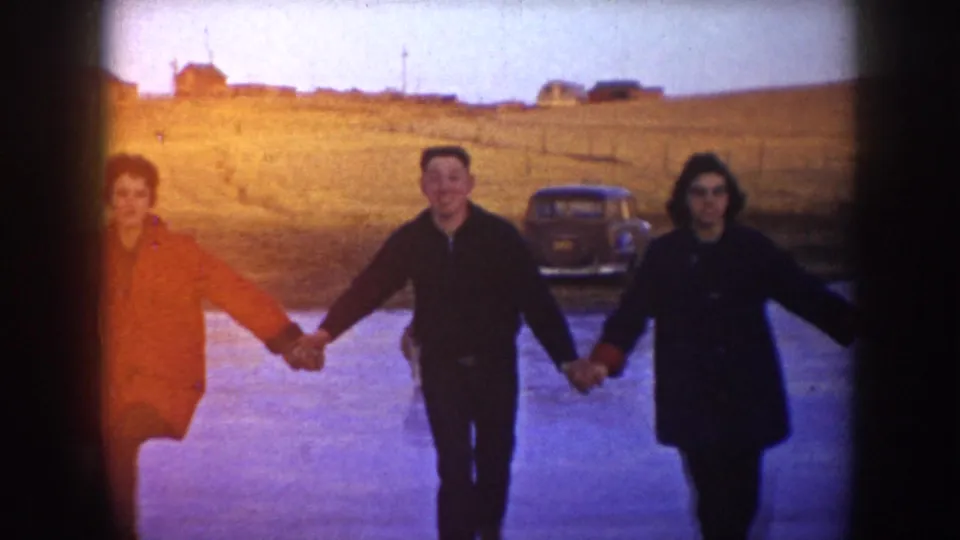 A closer 8mm frame shows three skaters holding hands on a frozen pond, with a mid-century car and open field behind them.