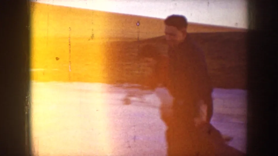 Two figures move on a frozen lake in supplied 1953 North Dakota footage, with one wearing a red winter jacket.
