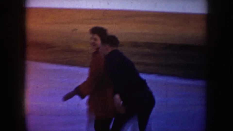 Two people, one in a red jacket, move together on the frozen lake in supplied 1953 North Dakota home-movie footage.