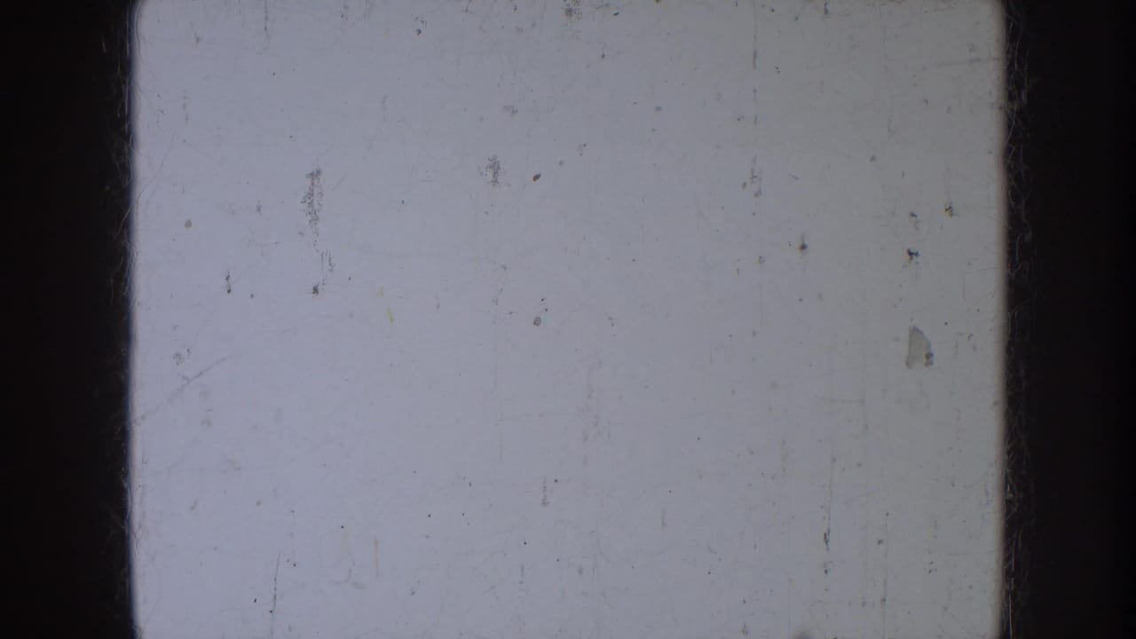 Pale blank 8mm film frame with dark borders, dust specks, and fine scratches.