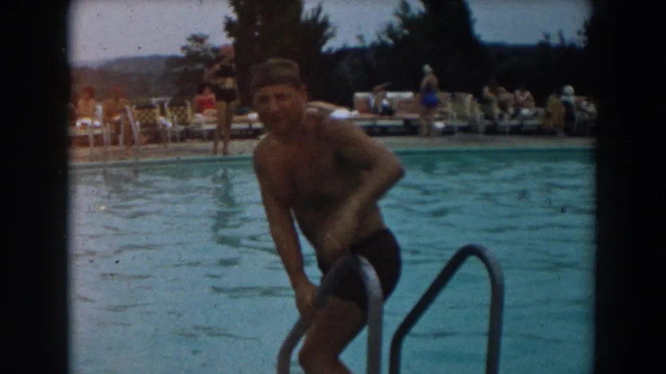 The man begins climbing down a metal pool ladder at an outdoor Los Angeles pool, with guests and lounge chairs behind him.