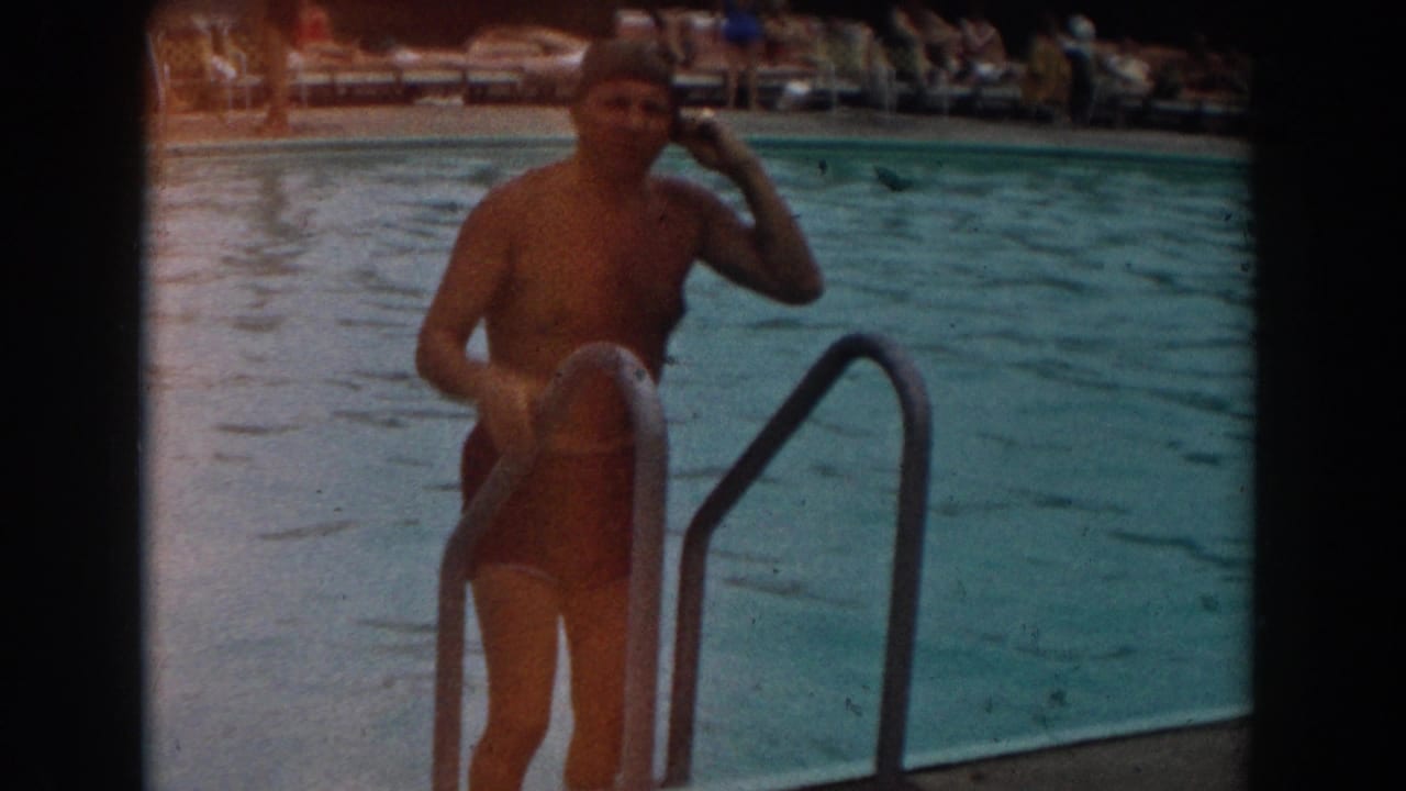 In 1961 Los Angeles footage, a man in a swim cap and trunks stands at a metal pool ladder before entering the water.