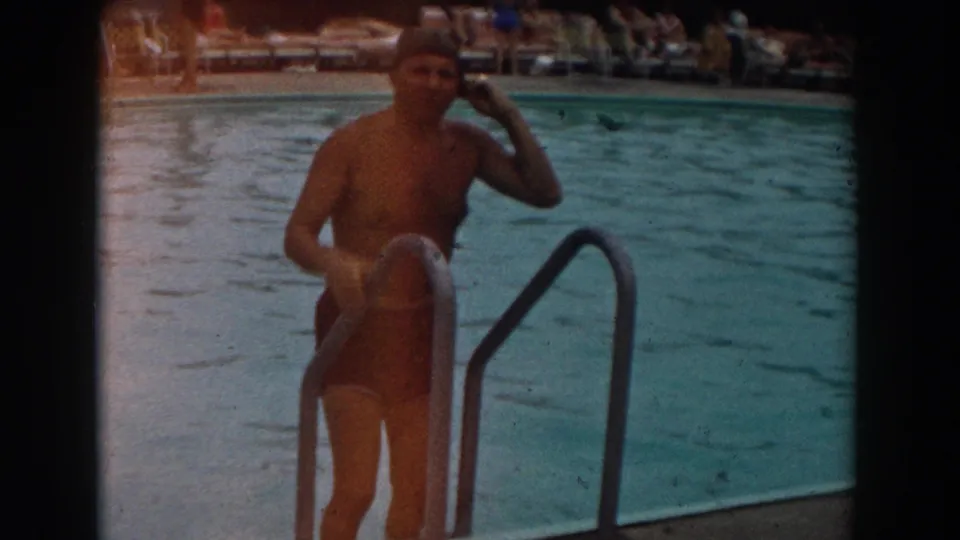 In 1961 Los Angeles footage, a man in a swim cap and trunks stands at a metal pool ladder before entering the water.